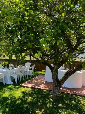 a table set up under a tree with white tables and chairs at Casa Lupe, retiro rural cerca de A Coruña in A Coruña