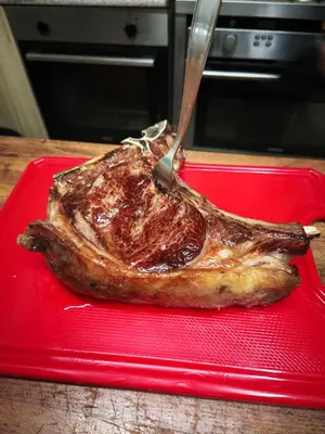 a piece of meat on a red plate with a knife at Pensión Palomos in San Xoán de Río