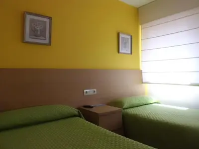 two beds in a room with yellow walls at Hostal Caracas in Lalín