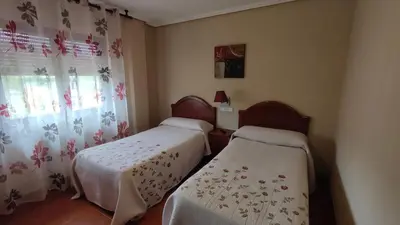 two beds in a room with curtains and a window at Pension Parrilla Casa Vicente in Tineo