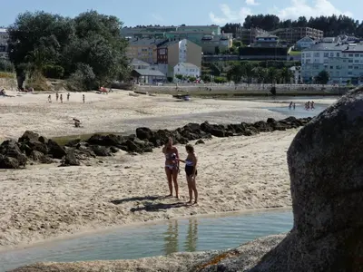 two women in bathing suits standing on a beach at Parque San Ciprián in San Ciprián