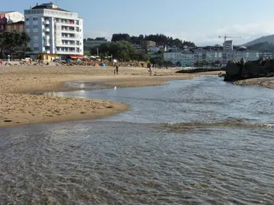 a beach with people walking on the sand and water at Parque San Ciprián in San Ciprián