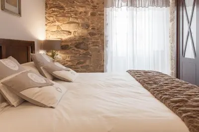 a large white bed in a bedroom with a stone wall at Nova Compostela Apartments in Santiago de Compostela