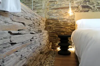 a bedroom with a bed and a stone wall at Hotel Apartamentos Casas da Fortaleza in Lugo