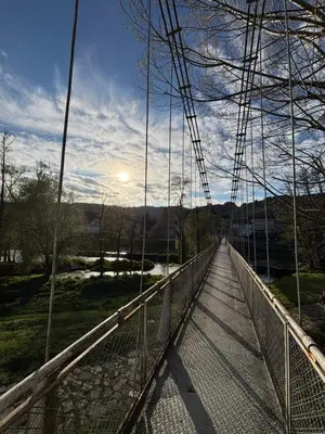 a suspension bridge over a river with the sun in the background at Piso Carballal, Fantástico piso en pleno centro in Leiro