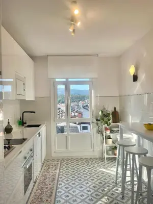 a white kitchen with a window and a counter with stools at O Victoriano in Caldas de Reis