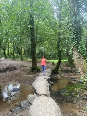 a woman walking across a rock bridge over a creek at Casa Victoriano in Melide
