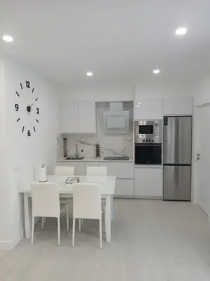 a white kitchen with a table and chairs and a clock at Alojamiento FCB Rúa Nova in O Pedrouzo