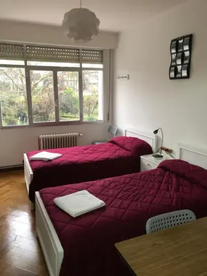 a bedroom with two beds with red sheets and a table at Hostal Costa Azul in Santiago de Compostela