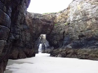 a rock wall with an arch in the middle of the water at Zona Las Catedrales Barreiros Playa de Altar in Villadaíde