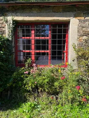 a red barred window in a brick building with flowers at O Freixo in A Capela