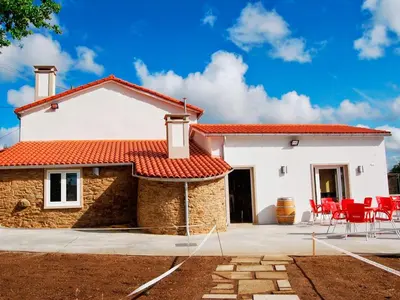 a white house with red roof and red chairs at Albergue Milpés in Ribadiso