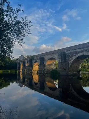a stone bridge with a reflection in the water at Roots and Boots in Lugo