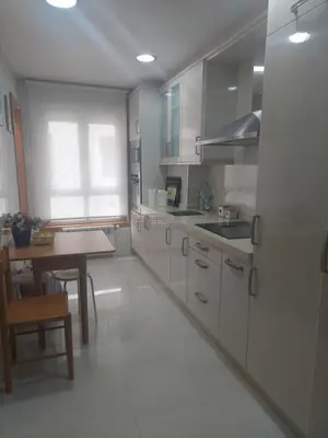 a kitchen with white cabinets and a wooden table at Apartamento Camino de Santiago in Ordes