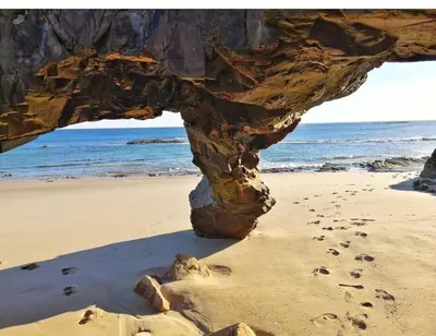 a rock formation on a beach with footprints in the sand at Apartamento Playa Foz 4 Dormitorios in Foz