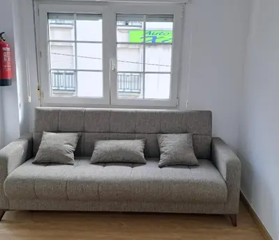a couch sitting in a room with two windows at Habitación privada en el mismo Camino de Santiago in Caldas de Reis