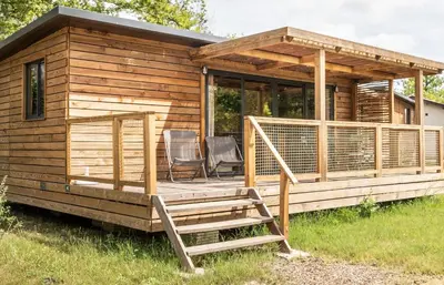 a large wooden cabin with a deck and chairs at Huttopia Caminos de Galicia in Prado