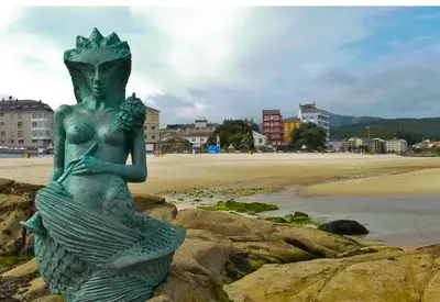 a statue of a mermaid sitting on some rocks near the beach at Atico Deluxe Limosa romántico moderno junto al mar in San Ciprián