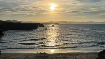 a sun setting over the ocean with a beach at Piso vacacional en Ribadeo in Ribadeo