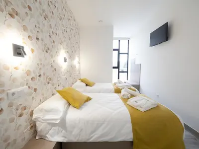 two beds in a bedroom with white walls and yellow pillows at Pensión Spa Cruceiro de Pedrouzo in O Pedrouzo