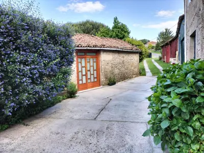 a stone building with a wooden door next to purple flowers at Casa do Ferrador in Penasillás