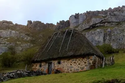 an old stone building with a grass roof on a field at La Vega De Somiedo 1 in Aguino