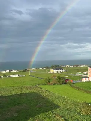 a rainbow in the sky over a green field at A Orillas de Llas in Foz