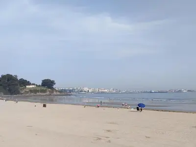 a beach with a group of people and a blue umbrella at housingcoruña BASTIAGUEIRO in Bastiagueiro
