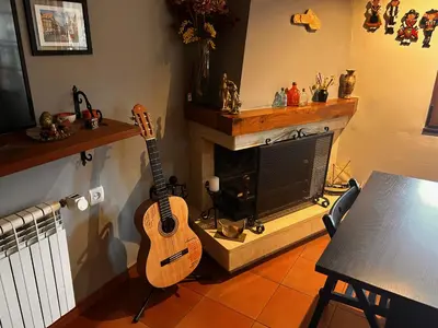 a guitar hanging on a wall in a living room with a fireplace at Hostal Casa San Nicolas in Molinaseca
