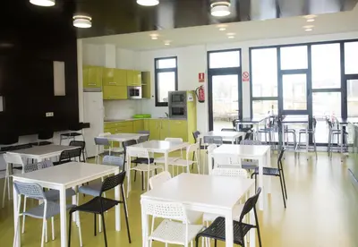 a cafeteria with white tables and chairs and windows at Albergue Spa Cruceiro de Pedrouzo in O Pedrouzo
