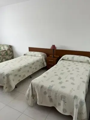 a bedroom with two beds and a chair and a table at Hostal Delfino in Bardaos