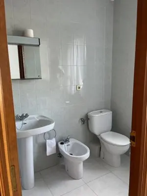 a white bathroom with a toilet and a sink at Hostal Delfino in Bardaos