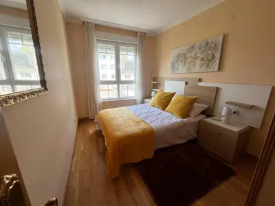 a bedroom with a bed with yellow sheets and two windows at Apartamento Los Gallegos in Foz