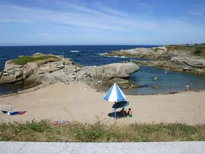 a beach with people on the sand and an umbrella at EnBURELA Playa in Burela de Cabo