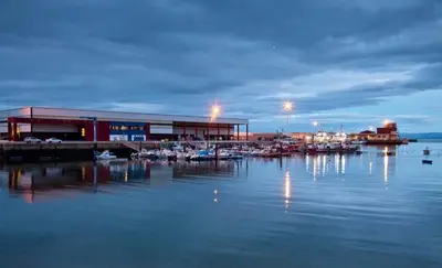 a marina with a building and boats in the water at EnBURELA Playa in Burela de Cabo