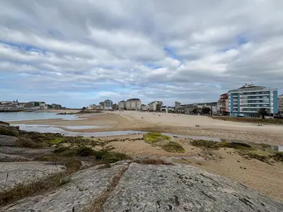 a sandy beach with buildings in the background at Ilusiones Da Mariña in San Ciprián