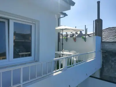 a white balcony with a table and an umbrella at Piso con terraza y garaje a un Paso de la Playa de Tapia in Tapia de Casariego