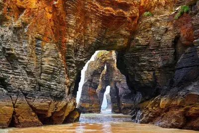 a cave in a rocky mountain with a waterfall at EnFOZ 1ª Línea de Playa II in Foz