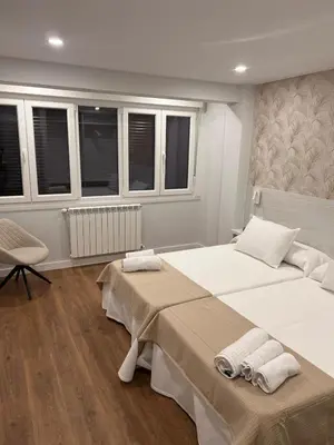 a bedroom with two beds and a chair and windows at Sleep Padrón in Padrón