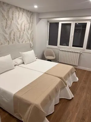 a bedroom with two beds and a chair and windows at Sleep Padrón in Padrón