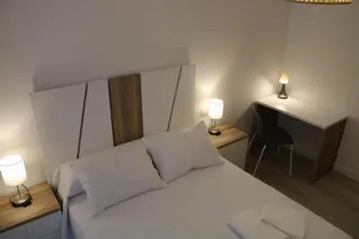 a bedroom with a white bed with two lamps and a desk at Alojamiento Doble R in Villalba