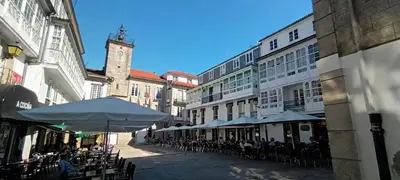 a street with tables and umbrellas and a clock tower at Adiva Loft in Puentedeume