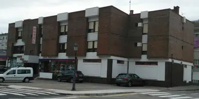 a brick building with cars parked in front of it at Hotel Puente de los Santos in Tapia de Casariego