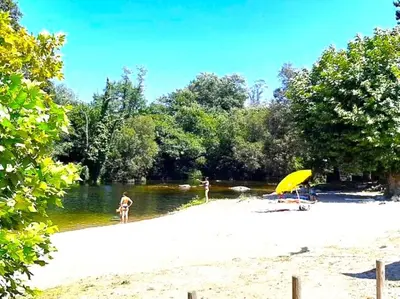 a beach with a yellow umbrella and people in the water at La Casa del Bosque del Agua y SPA Prexigueiro Obsequio entrada por persona a circuito termal in Mondariz