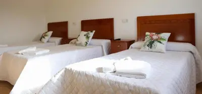 two beds in a room with white sheets and towels at Pension El Caminante in Portomarin