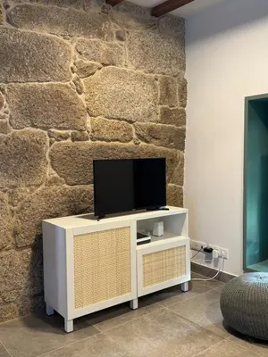 a tv on a white stand in front of a stone wall at A CASIÑA dos LARANXOS in Cenlle