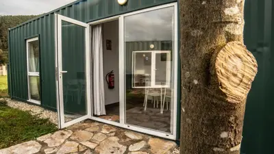 a green house with glass doors and a tree at Xeocámping Montañas do Courel
