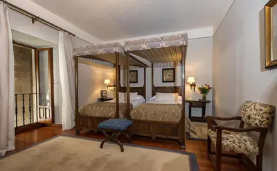 a bedroom with a four poster bed and a chair at Parador de Santiago - Hostal Reis Catolicos in Santiago de Compostela