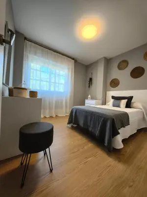 a bedroom with a bed and a stool and a window at Apart Martínez Rosalía in Padrón