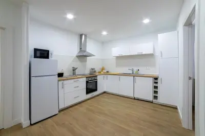 a white kitchen with white appliances and wooden floors at Nataly,s House in Tapia de Casariego